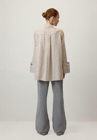 Svijetlosmeđa košulja s vertikalnim prugama, dugim rukavima i dugmadima na manžetama; uparen s razrokim, teksturiranim sivim hlačama. Jednostavan, minimalistički dizajn.