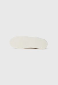 Zapatilla blanca con una suela de goma texturizada, que presenta un material superior liso y un diseño minimalista. Sin marcas ni patrones visibles.
