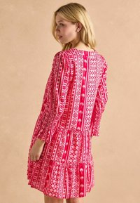 Różowa sukienka w kwiatowy wzór z długimi rękawami i warstwowym dołem, z marszczonym wykończeniem rękawów i pleców. Lekka tkanina.