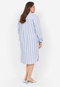 Gestreepte jurk met lange mouwen, met blauw-witte verticale strepen, zijsplitten en zachte stof. Gecombineerd met zilveren open teen hakken.