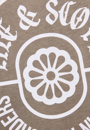 Wit bloemmotief met afgeronde bloemblaadjes binnen een ovaal, omringd door gedeeltelijke witte tekst op een beige stoffen achtergrond met textuur.