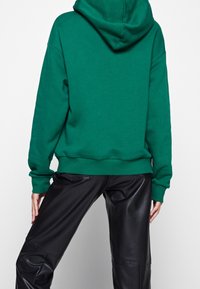 Grön huvtröja i mjukt material, med avslappnad passform och ribbade ärmslut, kombinerad med glänsande svarta läderbyxor.