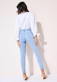 Vaaleansiniset korkeavyötäröiset skinny-farkut, joissa on sileä pinta, kaksi taka-taskua ja istuva malli yhdistettynä valkoiseen paitaan.