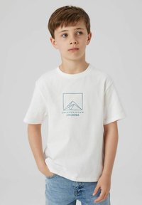 T-shirt en coton blanc avec un graphique géométrique de montagne bleue et le texte "DMS 35°00′N, 112°00′W ARIZONA" au centre. Manches courtes.