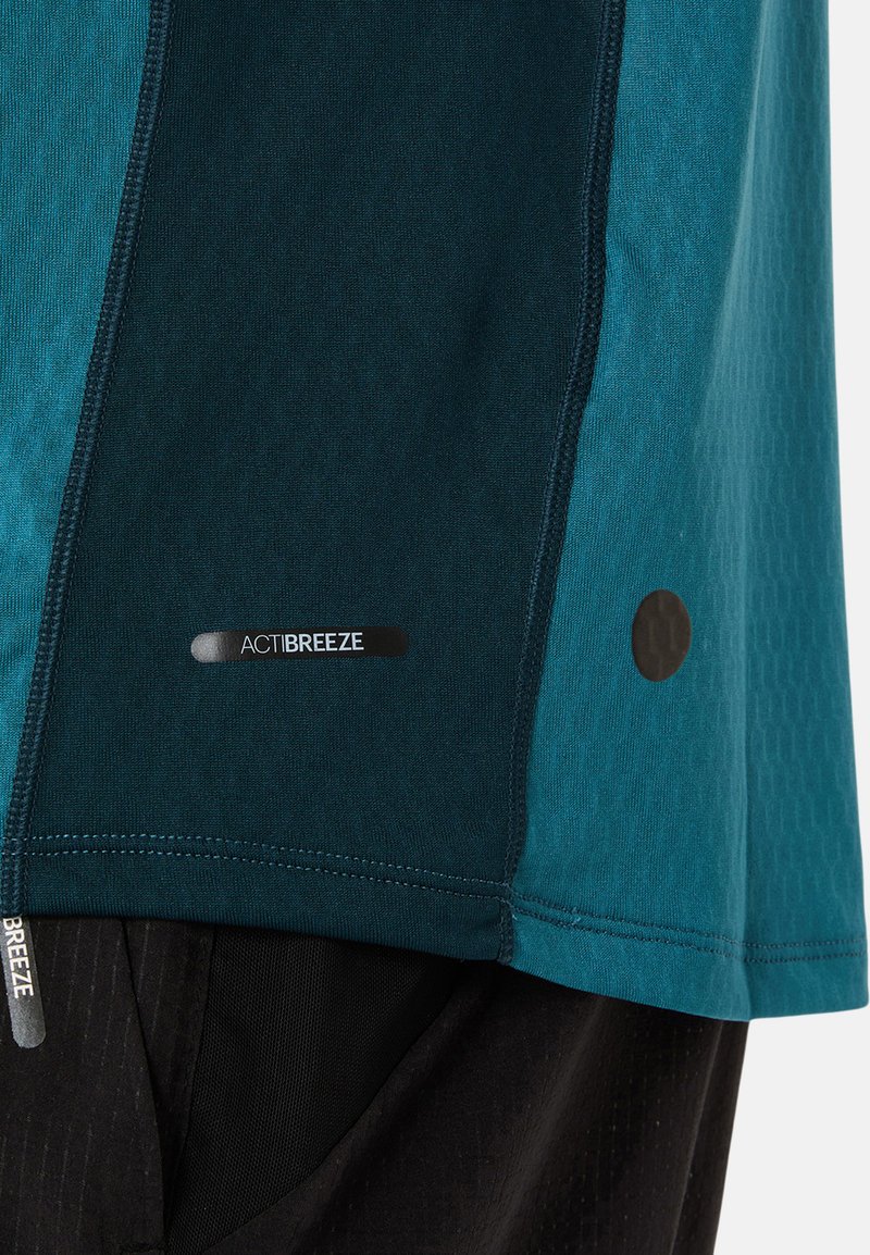 T-shirt de sport à manches courtes en tissu teal et vert foncé avec un motif texturé, arborant un logo "ACTIBREEZE" et des détails surpiqués.