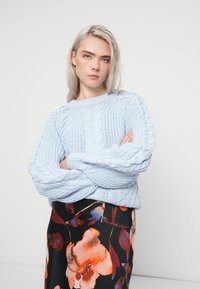 Maglione lavorato a maglia di un blu chiaro con un motivo a treccia testurizzato, abbinato a una gonna nera a fiori con accenti rossi e arancioni.