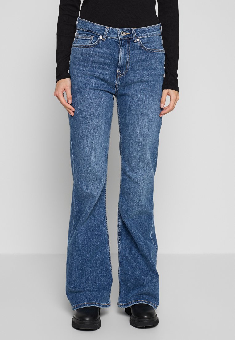 Jean évasés en denim, de couleur bleu avec un délavage moyen, cinq poches et une fermeture classique à bouton et zip.
