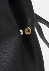 Czarna skórzana torba o teksturowanym wykończeniu, z detalami w złotym kolorze i dyskretnym otwarciem do mocowania.