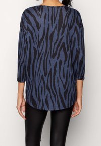 Blå och svart randig långärmad topp med avslappnad passform, rund halsringning och böjd fåll, kombinerad med svarta leggings.