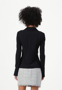 Blusa nera aderente con colletto e maniche lunghe, abbinata a una gonna grigia strutturata con orlo frangiato.