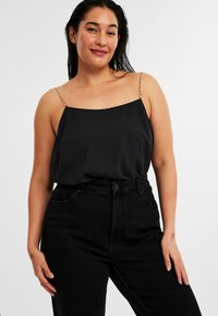 Svart siden top med fyrkantig halsringning och delikata guldkedjor, matchad med högmidjade svarta jeans. Slät textur, minimalistisk design.