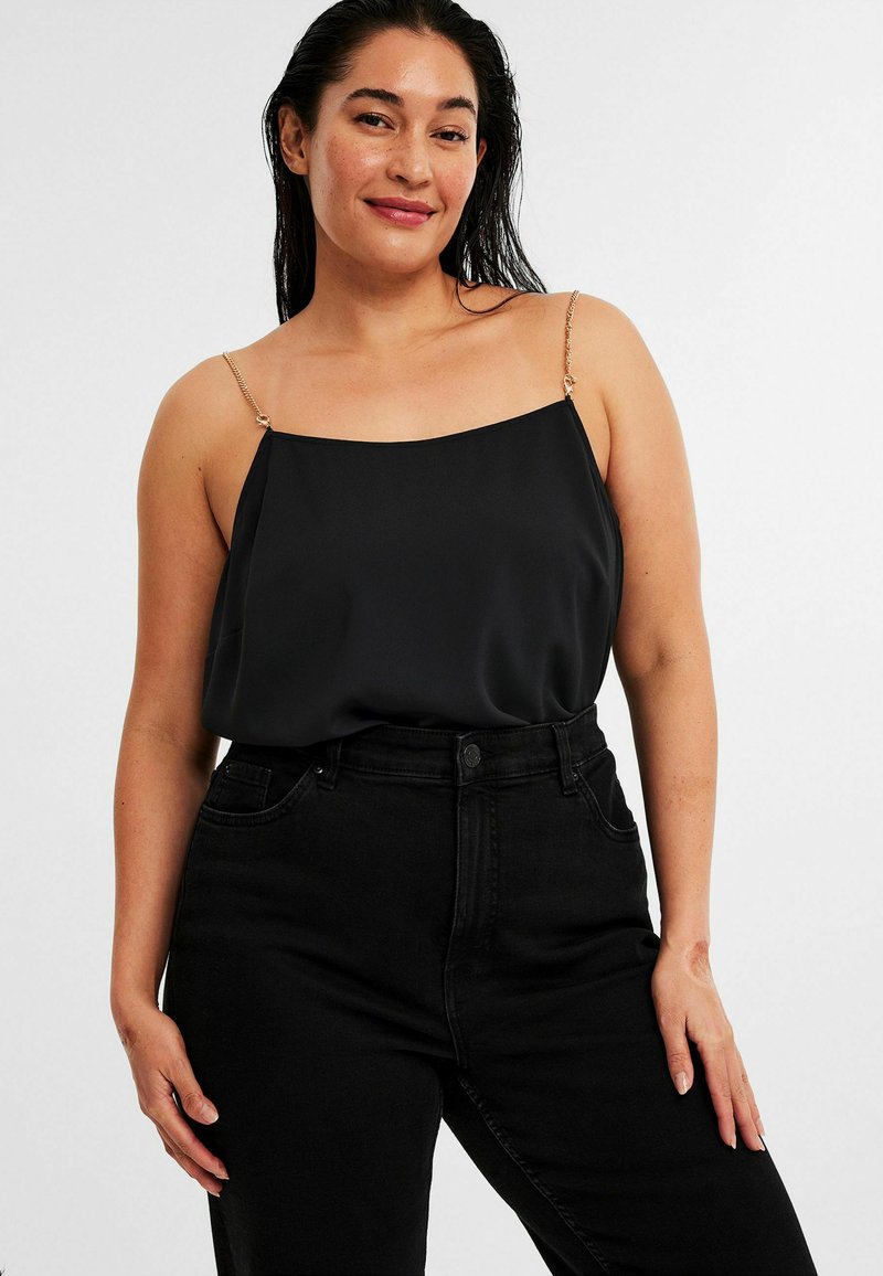 Svart siden top med fyrkantig halsringning och delikata guldkedjor, matchad med högmidjade svarta jeans. Slät textur, minimalistisk design.
