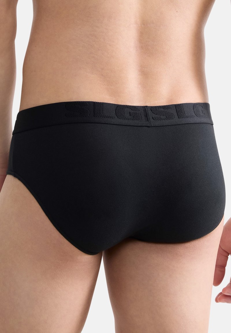 Slip noir en tissu lisse, avec une ceinture élastique embossée du logo et une coupe ajustée.