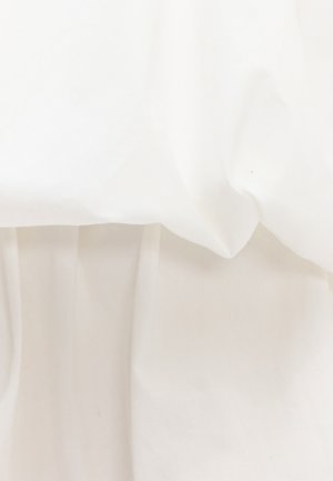 Tela blanca con pliegues suaves y sombras delicadas, destacando la textura y el juego de luces sobre una superficie lisa.