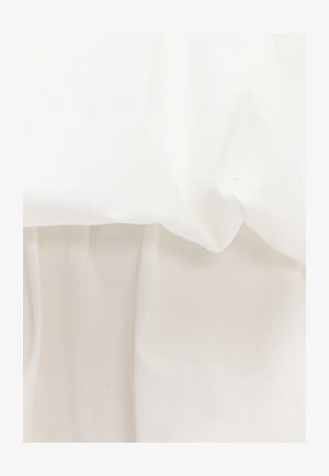 Tela blanca con pliegues suaves y sombras delicadas, destacando la textura y el juego de luces sobre una superficie lisa.