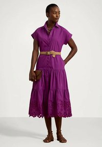 Violetinis medvilninis suknelė-suknelė trumpomis rankovėmis, su sluoksniuota sijonu ir siuvinėtu nėriniu. Dėvima su pintu diržu ir rudu krepšiu.