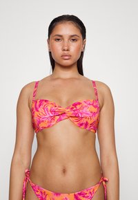 Conjunto de biquíni floral com um design de frente torcida. Tecido laranja vivo com padrões de folhas rosa. Alças ajustáveis e laços laterais nos calções.