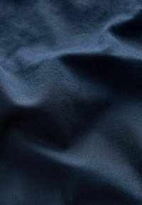Tessuto blu navy con una texture liscia, caratterizzato da leggere ondulazioni e una morbida lucentezza. Il materiale sembra essere cotone o un misto cotone.