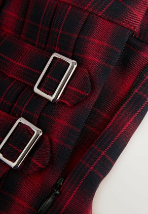 Material în carouri roșii și negre cu catarame metalice argintii și un fermoar. Are o suprafață texturată și linii de model distincte.