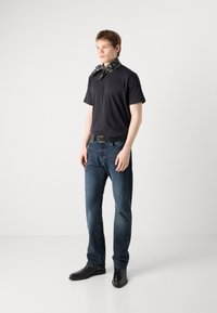 Černé tričko s krátkým rukávem, modré džínové kalhoty, černé kožené kotníkové boty a šátek s vzorem uvázaný kolem krku. Neformální outfit.
