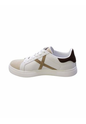 Zapatilla blanca de perfil bajo con puntera beige, parche marrón en el talón y detalle "X" beige en el lateral con cordones y suela blanca.