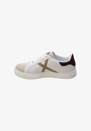 Sneaker bianco low-top con punta beige, toppa marrone sul tallone e dettaglio "X" beige sul lato con lacci e suola bianchi.
