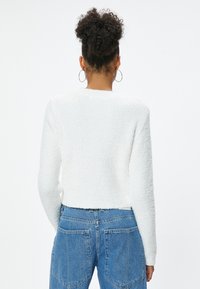 Witte, gestructureerde, cropped trui met lange mouwen, voorzien van een ronde halslijn, gecombineerd met high-waisted blauwe denim jeans.