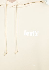 Hoodie beige avec une capuche à cordon de serrage, présentant un logo Levi's blanc sur la poitrine gauche. Texture douce et poignets côtelés.