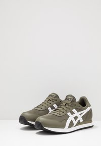 Oliwkowo-zielone buty sportowe z białymi akcentami, siateczkową i syntetyczną cholewką, płaską czarną gumową podeszwą oraz klasycznym wiązaniem na sznurowadła.