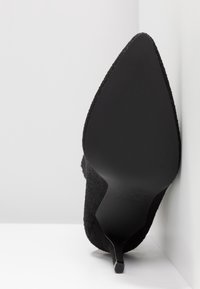 Schwarzer Absatzschuh mit spitzem Zehenbereich und strukturierter Oberseite aus Stoff. Die Sohle ist glatt mit einem schlanken, sich verjüngenden Absatz.