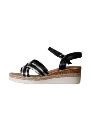 Sandalia cuña con tiras negras y plateadas con hebilla en el tobillo, plantilla intermedia de corcho y cuerda trenzada, y suela exterior de goma blanca texturizada.