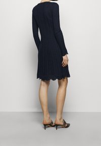 Námořnická modrá pletená šaty s dlouhými rukávy, zdobené texturovaným kabelovým vzorem a rýhovaným lemem. Nosit s botami na otevřeném podpatku.