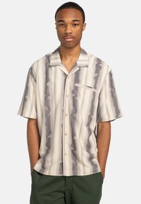 Short-sleeve shirt in cream and gray with wavy striped pattern, featuring a button-down front and a chest pocket. Made from lightweight fabric.