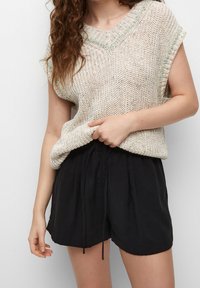 Top de punto beige claro con un acento verde alrededor del cuello, combinado con pantalones cortos negros con cordón. Ajuste relajado, mangas cortas, tela texturizada.