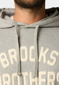 Hoodie in cotone grigio con tasca a marsupio, caratterizzato da un ricamo in crema testurizzato che riporta la scritta "BROOKS BROTHERS" sul petto.