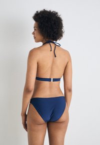 Navy bikini-set med halterneck med bånd, justerbart ryggbånd med metallkrok, og lavt skjært bikinitopp, alt laget av glatt stoff.