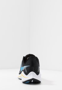 Scarpa sportiva nera con accenti blu e bianchi, esposta su uno sfondo bianco semplice, mettendo in evidenza il suo design e la sua struttura posteriori.