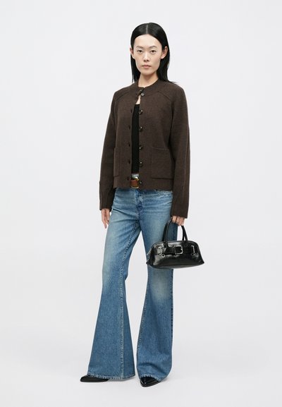 Cardigã castanho texturado com gola redonda e botões, combinado com jeans azuis claros flare. Modelo segura uma pequena bolsa preta.