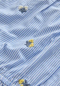 Blue and white striped fabric with small embroidered flowers in yellow, gray, and white scattered across the surface.