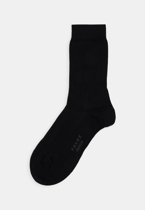 Chaussette noire en matériau lisse et extensible. Dotée d'une bordure côtelée, d'un talon et d'un orteil renforcés. Marque imprimée sur la semelle.