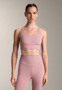 Ružový športový podprsenka s okrúhlym výstrihom a širokými ramienkami, v kombinácii s ladnými legínami s vysokým pásom, ktoré majú hladkú, elastickú štruktúru.