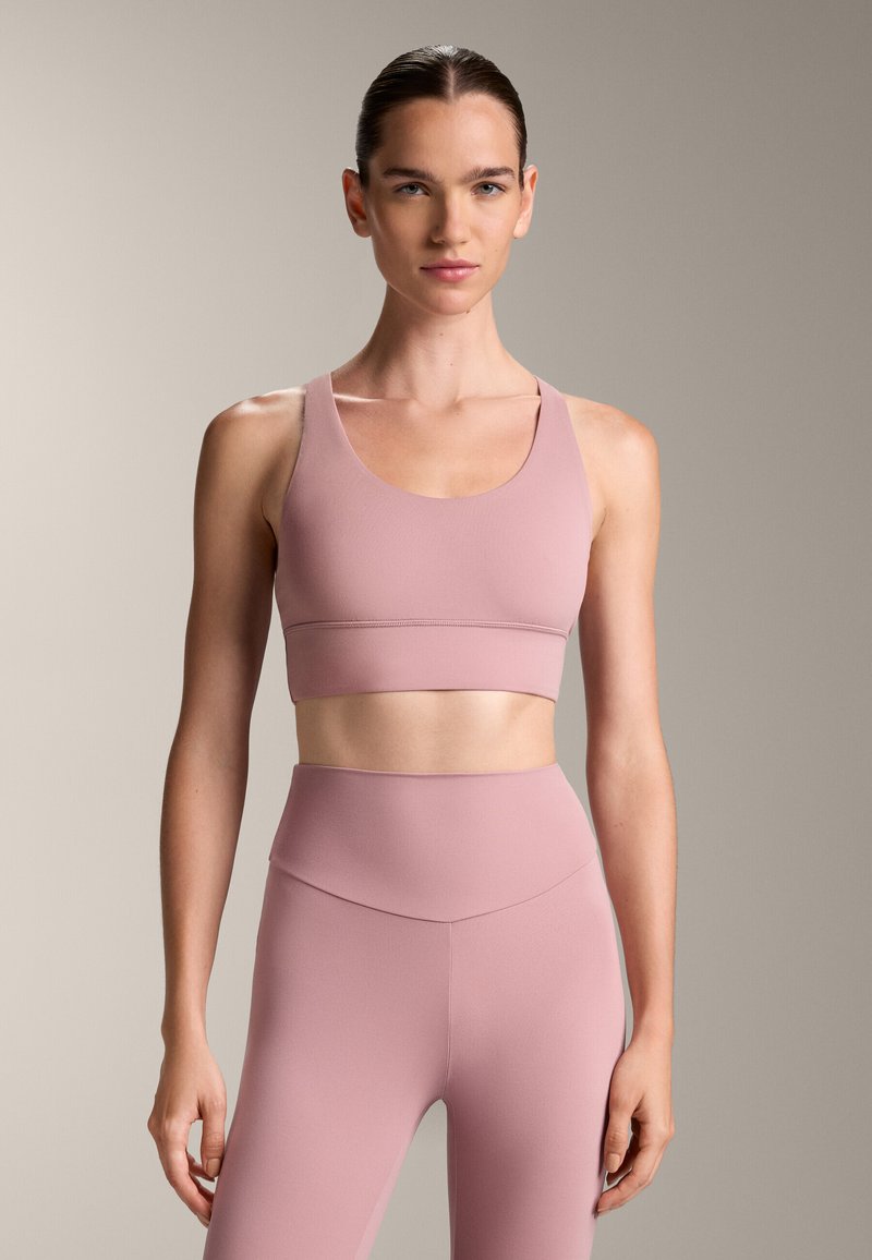Ružový športový podprsenka s okrúhlym výstrihom a širokými ramienkami, v kombinácii s ladnými legínami s vysokým pásom, ktoré majú hladkú, elastickú štruktúru.
