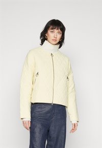 Gepolsterte gelbe Jacke mit cropped Design, hochgeschlossenem Kragen, silbernem Reißverschluss und zwei seitlichen Reißverschlusstaschen. Strukturiert.