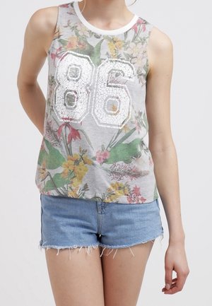Mouwloos grijs topje met witte "86" en kleurrijke bloemenprint, gecombineerd met versleten denimshorts, gedragen door een persoon met de handen achter de rug.