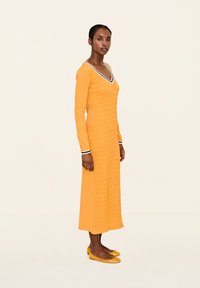 Langärmliges Kleid mit V-Ausschnitt in leuchtendem Gelb und strukturiertem, gerafftem Design. Besitzt einen kontrastierenden schwarz-weißen Rand am Ausschnitt.