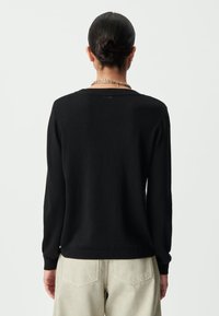 Maglione nero con maniche lunghe e scollo rotondo, realizzato in un materiale morbido. Presenta un'etichetta di branding discreta sul retro del collo.