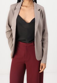 Ljusgrå kavaj med skräddarsydd passform, matchad med en svart satinkamer och bordeauxfärgade byxor med hög midja. Slät textur, klassisk design.