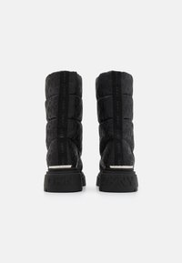 Fekete puffert boots DKNY logómintával, magas szárú, texturált gumitalppal, amelyen felirat található a sarkon. Sima szövetfelület.