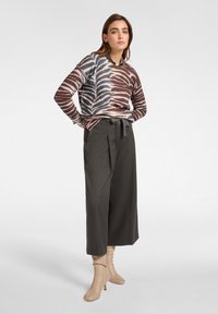 Pullover mit einem braun-blauen Blättermuster, kombiniert mit hochgeschnittenen, grauen weit geschnittenen Hosen und beige Knöchelstiefeln mit blockiertem Absatz.