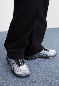Scarpe sportive con un design grigio e nero, dotate di una tomaia testurizzata, un motivo distintivo e lacci visibili; abbinate a pantaloni neri.